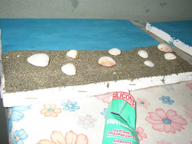 Aggiungiamo le conchiglie fissandole con del silicone trasparente Aggiungiamo le conchiglie fissandole con del silicone trasparente