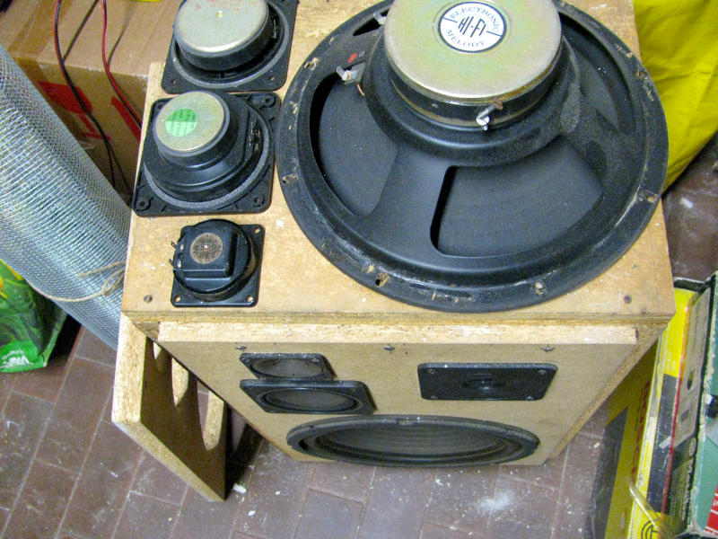Altoparlanti di recupero a tre vie per cassa amplificata karaoke fai da te: woofer 25cm, midrange e tweeter Vista dall'alto degli altoparlanti di recupero utilizzati nel progetto: woofer a sospensione pneumatica da 25cm, midrange quadrato e tweeter piezoelettrico smontati dalla vecchia cassa acustica. Sul lato sinistro è visibile la rete metallica di protezione arrotolata. Sullo sfondo la vecchia cassa acustica originale