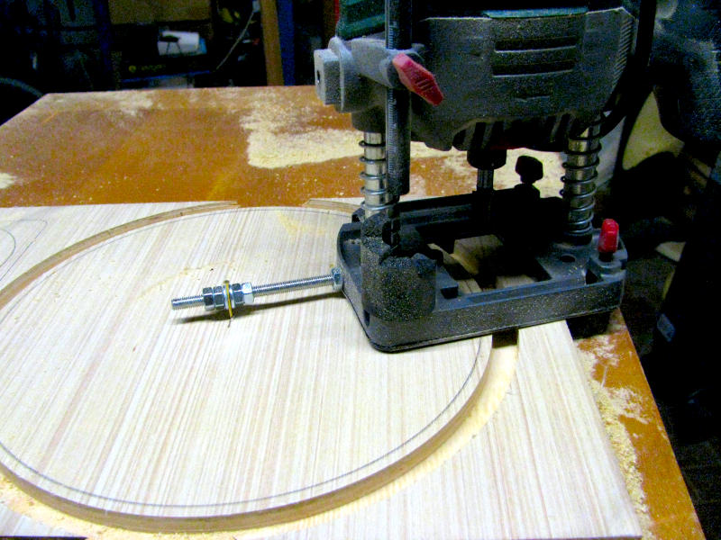 Fresatura circolare dell'incasso del woofer da 25cm con sistema di guida artigianale su tondino filettato Dettaglio della fresatura circolare dell'incasso per il woofer da 25cm sul pannello frontale della cassa acustica. La fresatrice a mano è guidata da un tondino filettato avvitato nella base dello strumento e fissato al centro del cerchio tramite dado e chiodino, creando un sistema di guida circolare artigianale che consente di fresare l'incasso con precisione. Sono ben visibili il solco già fresato e la segatura prodotta dall'operazione