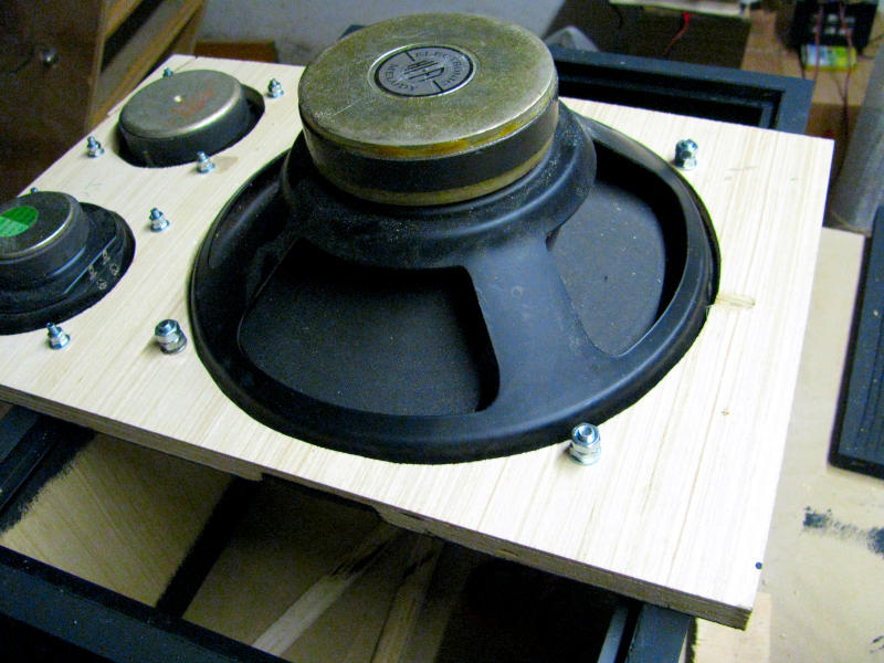 Montaggio degli altoparlanti sul pannello frontale della cassa acustica karaoke con viti passanti e controdadi Vista dall'alto del pannello frontale della cassa acustica per karaoke con i tre altoparlanti montati e fissati con viti passanti e controdadi: il woofer a sospensione pneumatica da 25cm al centro occupa la maggior parte del pannello, il midrange quadrato in alto a sinistra e il tweeter piezoelettrico in basso a sinistra. I controdadi visibili intorno a ciascun altoparlante garantiscono la tenuta del fissaggio nonostante le vibrazioni.