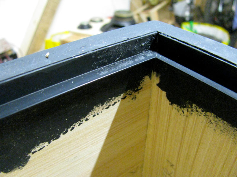 Profilato ad L in plastica nera e bordino paraspifferi in gomma per il fissaggio ermetico del pannello frontale Dettaglio del profilato ad L in plastica nera da 10x10mm incollato lungo il bordo interno della cassa acustica per karaoke. Il profilato funge da battuta per il pannello frontale e nasconde le graffe di fissaggio della rete metallica. Sul lato orizzontale del profilato è visibile il bordino in gomma paraspifferi che garantisce la tenuta ermetica della cassa.