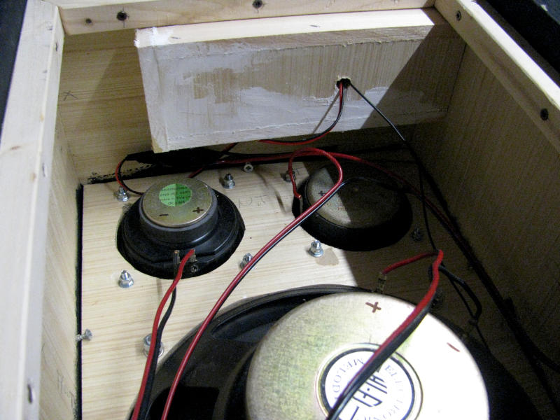 Scatola interna per la tenuta ermetica sotto la scheda amplificatore e cablaggio degli altoparlanti Vista interna della cassa acustica per karaoke con la piccola scatola in legno costruita per isolare il vano della scheda amplificatore dal volume interno della cassa. In primo piano sono visibili il midrange e il tweeter montati sul pannello frontale visti dal retro con i cavi di collegamento rossi e neri. In basso a destra è visibile parzialmente il magnete del woofer da 25cm. La scatola in alto garantisce la tenuta ermetica necessaria per il corretto funzionamento del woofer a sospensione pneumatica.