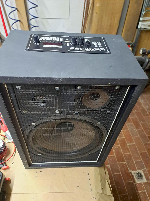 Cassa amplificata per karaoke fai da te completata: woofer 25cm, scheda amplificatore Bluetooth e rete metallica di protezione Vista frontale della cassa amplificata per karaoke fai da te completamente assemblata e verniciata di nero opaco. Il pannello frontale mostra la rete metallica di protezione che copre il woofer da 25cm in basso e i due altoparlanti più piccoli in alto. Nel pannello superiore è integrata la scheda amplificatore Bluetooth con ingresso microfono, display LED e controlli del volume. Il profilato nero perimetrale incornicia il pannello frontale conferendo un aspetto ordinato e professionale.