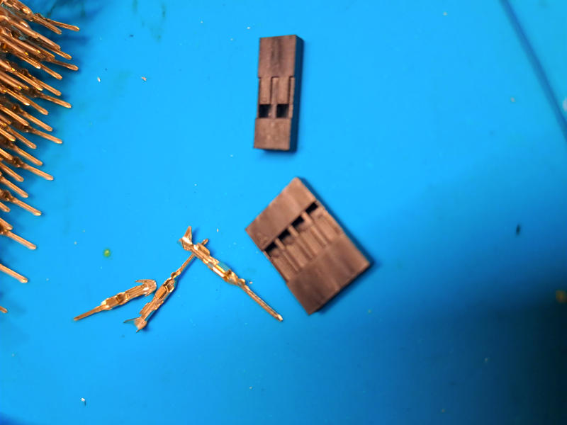 I componenti dei connettori Dupont passo 2,54mm prima della crimpatura: la scocca a quattro poli (in basso a destra), la scocca a due poli (in alto) e alcuni contatti metallici dorati pronti per essere crimpati sui fili