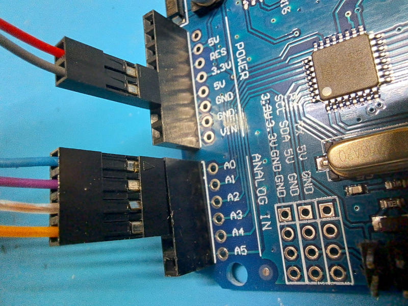 Dettaglio del collegamento dei due connettori Dupont passo 2,54mm sulla scheda Arduino Uno: il connettore a due poli inserito sui pin 5V e GND della sezione POWER (in alto) e il connettore a quattro poli inserito sui pin A0÷A3 della sezione ANALOG IN (in basso). Sullo sfondo sono visibili il microcontrollore ATmega328P e il quarzo della scheda