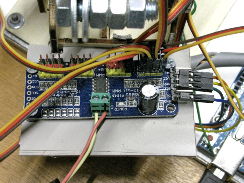 Vista dall'alto della scheda driver PCA9685 collegata ai servomotori del braccio robotico. Il connettore verde in basso è il morsetto di alimentazione esterna per i servomotori, mentre i connettori Dupont sul lato destro portano i segnali I2C (SDA e SCL) verso Arduino Uno, visibile parzialmente in basso a destra. In alto sono visibili i connettori a tre poli gialli per il collegamento dei servomotori