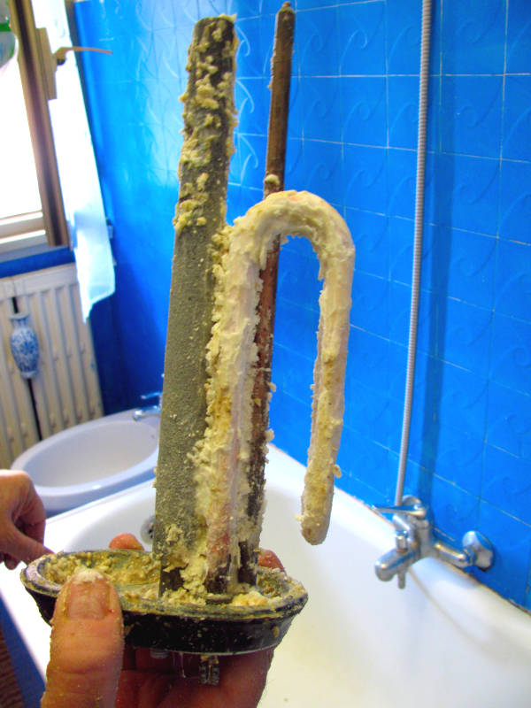 Foto della resistenza dello scaldabagno appena smontata, completamente ricoperta da uno spesso strato di calcare che ne riduce l’efficienza termica e può causarne il surriscaldamento e la rottura