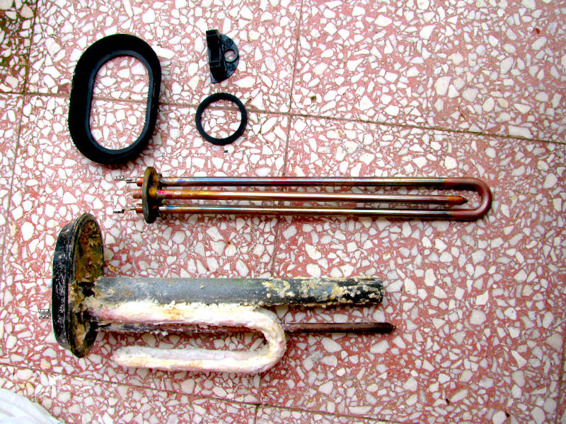 Foto dei componenti dello scaldabagno affiancati: sotto i pezzi vecchi usurati, come resistenza e anodo consumati, e sopra i ricambi nuovi pronti per la sostituzione, per evidenziare la differenza di stato e l’importanza della manutenzione